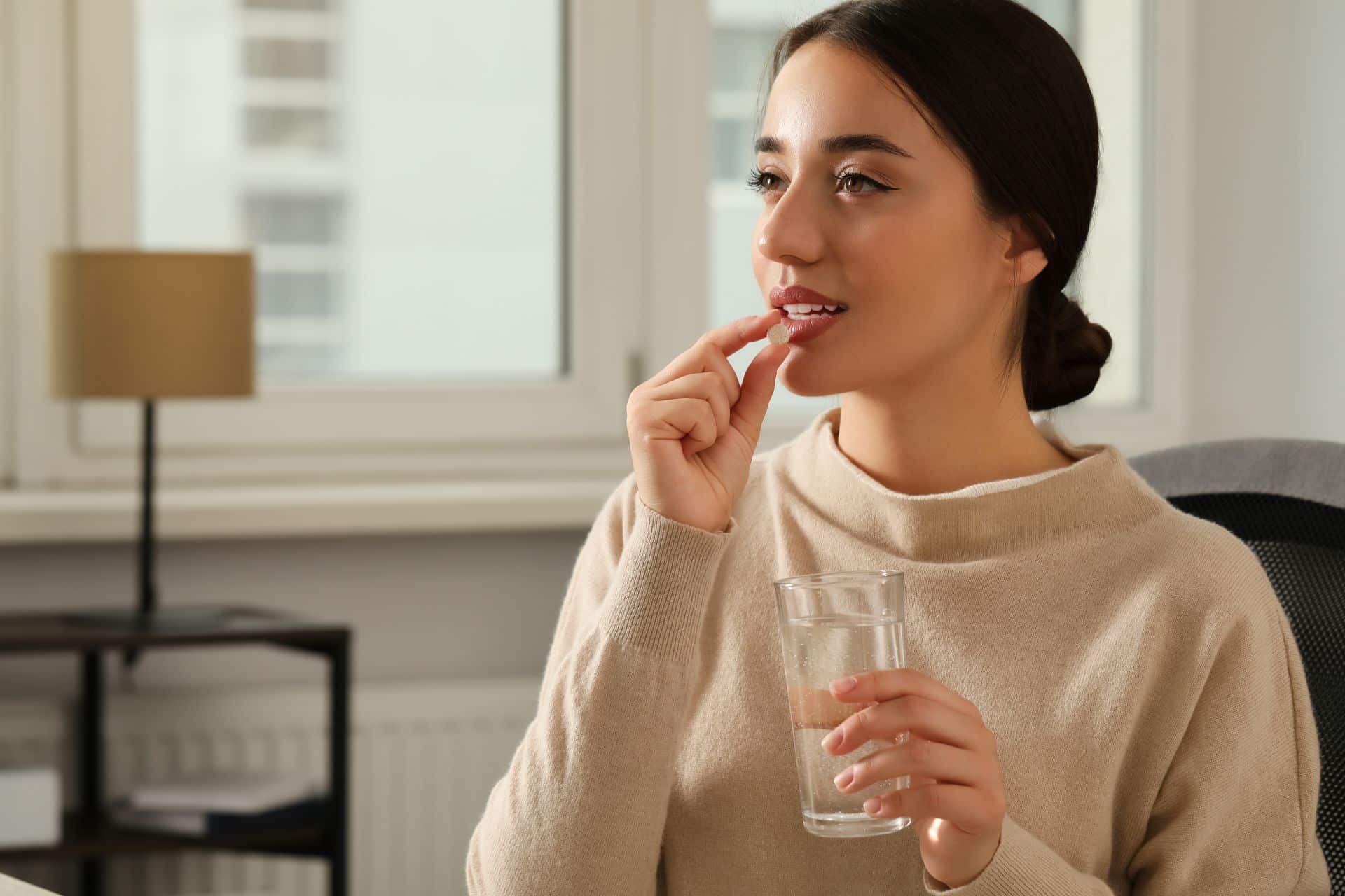 Junge Frau nimmt mit einem Glas Wasser eine Kapsel als Nahrungsergänzung mit krillöl zur Unterstützung bei stillen Entzündungen